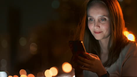 A-young-woman-in-the-night-city-looks-at-the-smartphone-screen-and-writes-a-text-message-communicates-in-social-networks-publishes-and-comments-on-photos